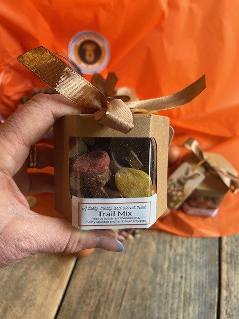 Box of 'Trail Mix' with a ribbon held by a hand against an orange background